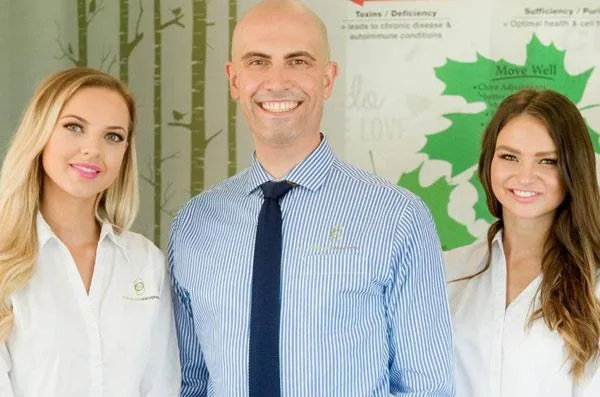 Three chiropractors standing near chiropractic tables in a clinic, discussing chiropractic techniques and treatments.